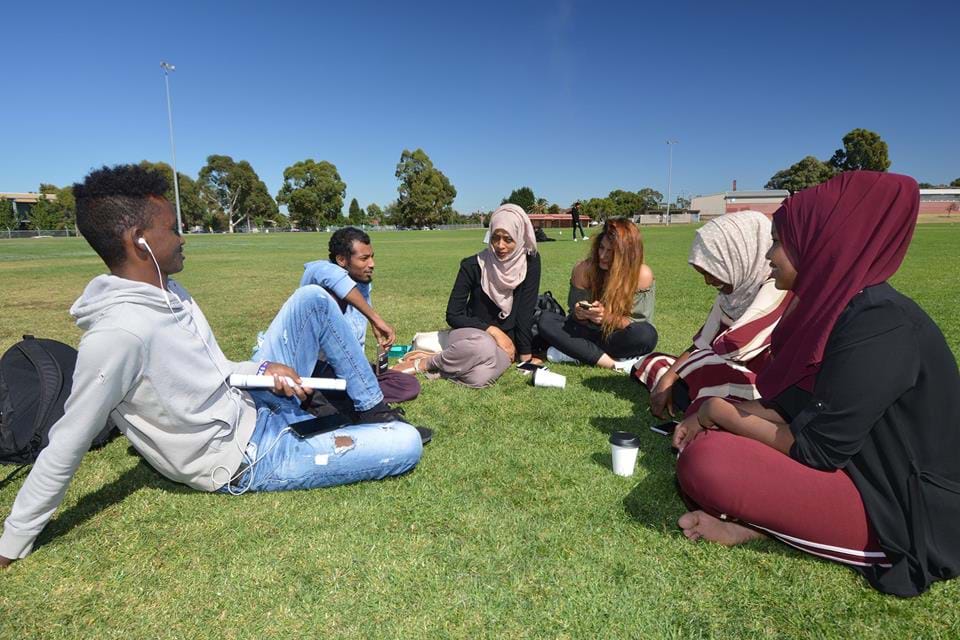 Students sitting on grass oval at campus