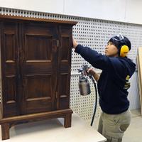 Carpentry student with compressed air lacquer gun and small free standing cabinet