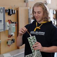 Electronics and Electrical student smiling while holding an electrical cord at a fuse box