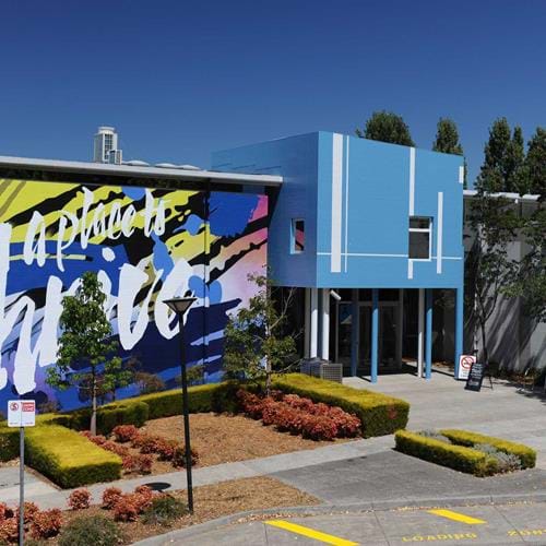 Facade of Greensborough campus. The entry is a blue building with a large mural that says "a place to thrive" on a blue, pink and yellow background