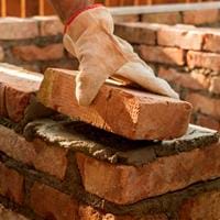 A person laying a brick on top of some mortar 
