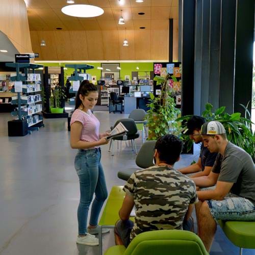 Image of Epping Library with students sitting down on couch and one student standing with newspaper