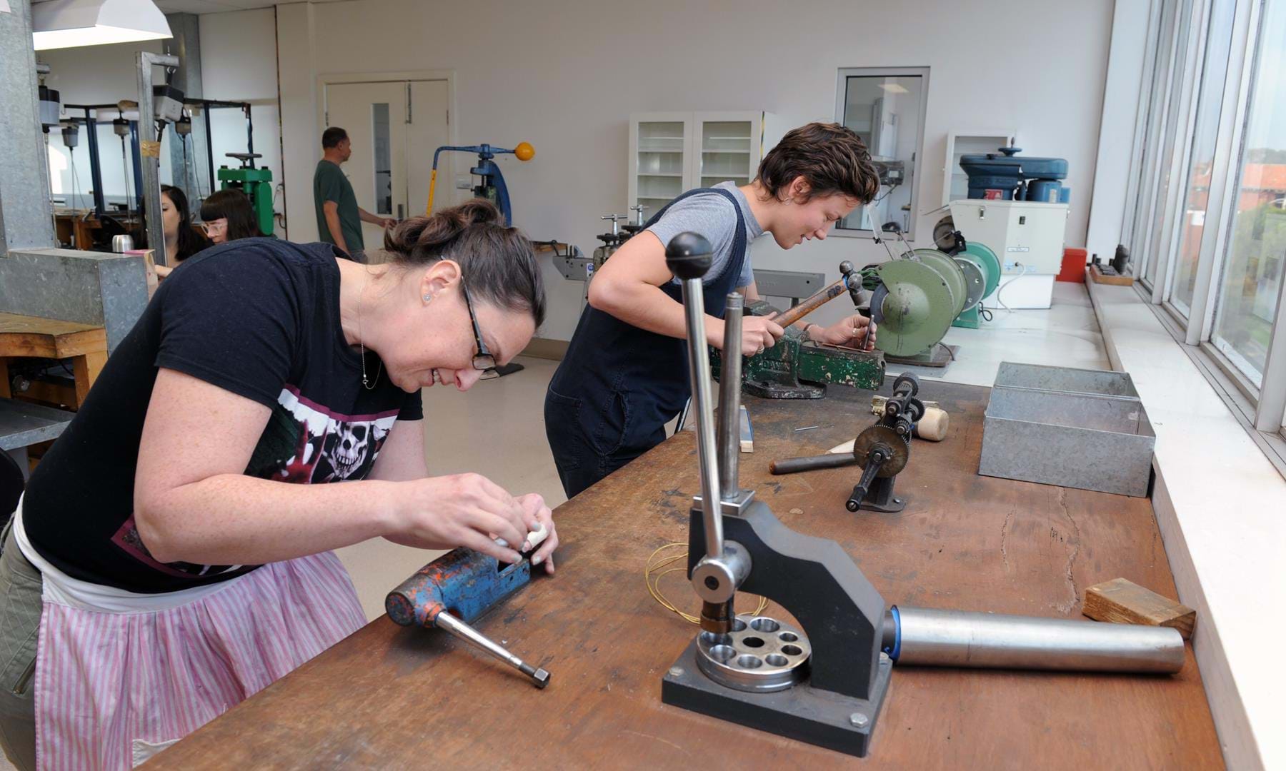 Two jewellery students working with items in vices in the jewellery workshop